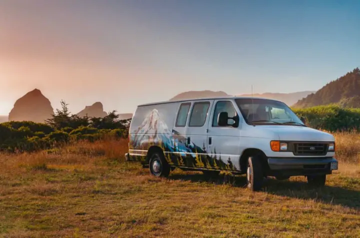 White Ford Econoline **RV rental** van featuring mountain art, parked in a scenic field with ocean rocks at sunset.. Ford Econoline E250supercab 2006