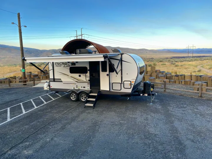 Modern RV rental with awning extended on a paved lot, overlooking a scenic, arid mountain landscape. Perfect for outdoor escapes!. Flagstaff Micro Lite 2021
