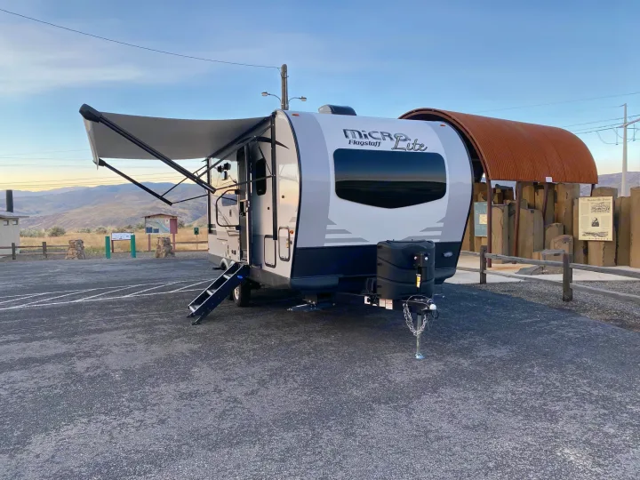 RV rental ready: A modern white and gray Micro Flagstaff Lite travel trailer with its awning extended, parked at a scenic overlook.. Flagstaff Micro Lite 2021