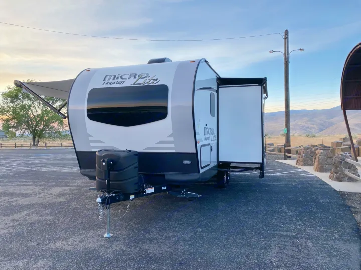 White and grey Micro Lite Flagstaff rv rental travel trailer parked with awning extended, door open, ready for adventure.. Flagstaff Micro Lite 2021
