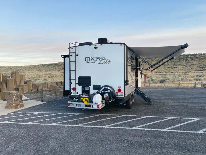A Micro Lite rv rental is parked in a desert lot, awning extended, with a generator on its rear cargo rack.. Flagstaff Micro Lite 2021