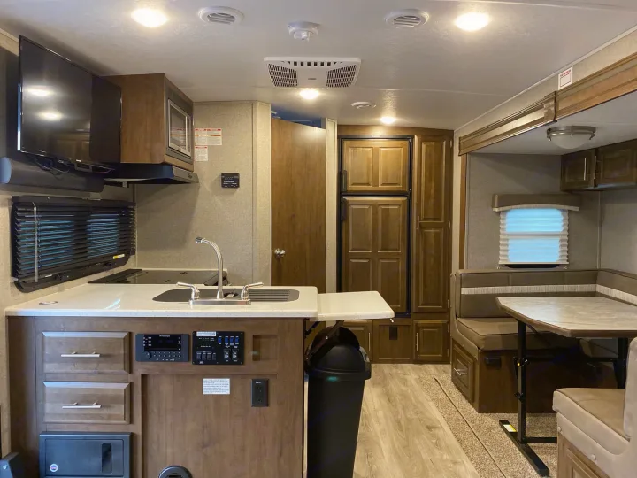 RV rental interior: a fully equipped kitchen area with a sink, stove, microwave, and TV, plus a cozy dining booth with table.. Flagstaff Micro Lite 2021