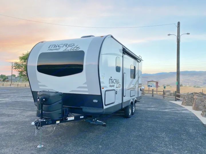 A pristine white and grey Micro Flagstaff Lite travel trailer (RV rental) sits in a paved lot at sunset.. Flagstaff Micro Lite 2021