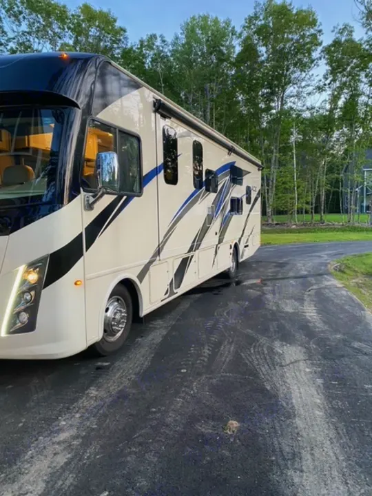 Spacious beige and black RV parked on an asphalt driveway. Consider this comfortable RV rental for your travels!. Thor Motor Coach A.C.E 2021
