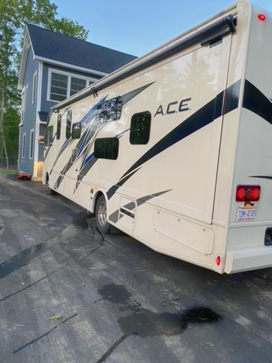 A spacious A.C.E. rv rental is parked on an asphalt driveway, offering a view of its side and storage areas.. Thor Motor Coach A.C.E 2021