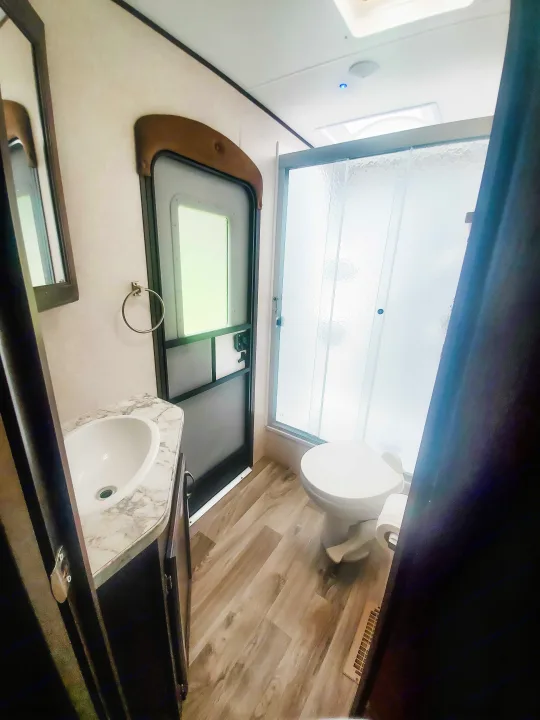 An RV rental's compact bathroom features a vanity with sink, a white toilet, and a shower with textured glass.. Jayco Jay Flight 2018