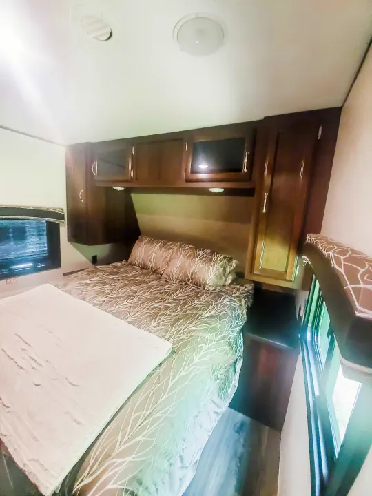 RV rental bedroom featuring a comfy bed with patterned bedding, overhead cabinets, and a window.. Jayco Jay Flight 2018