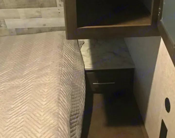 Inside a compact RV rental, featuring a comfortable bed with chevron quilt and a built-in nightstand.. Coleman 285BH 2021