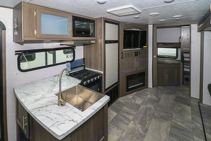 Discover this RV rental's modern interior, featuring a well-equipped kitchen, TV living area, and a cozy bunk space.. Dutchmen Kodiak 2021