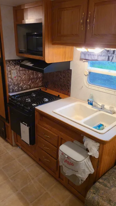 Functional RV rental kitchen with oak cabinets, stovetop, double sink, microwave, and copper backsplash.. Dutchmen Lite 2003