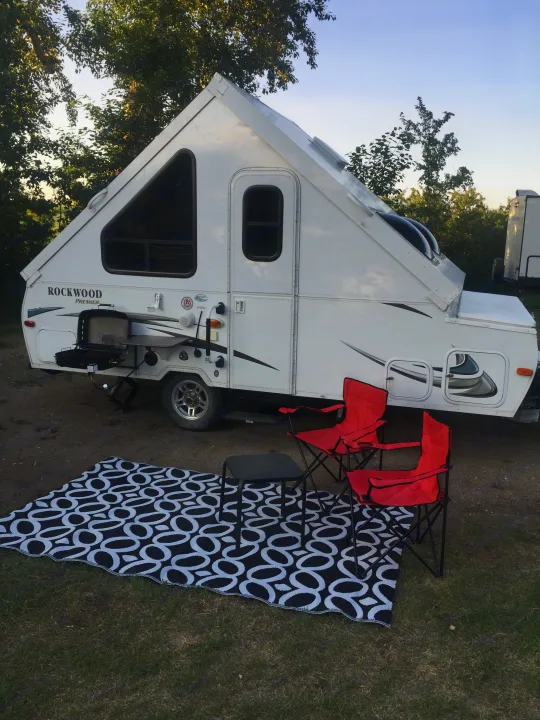 A cozy A-frame RV rental set up at a campsite, featuring a black and white rug and red chairs.. Forest River Rockwood 2014