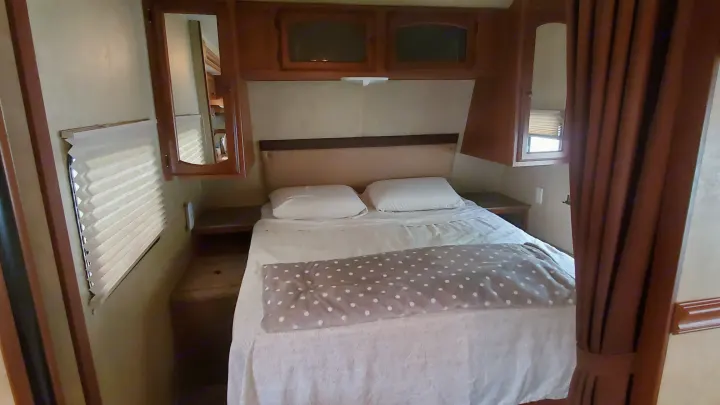 Inside an RV rental: a compact bedroom featuring a comfortable bed, overhead cabinets, and window blinds.. Dutchmen Dutchmen 2012