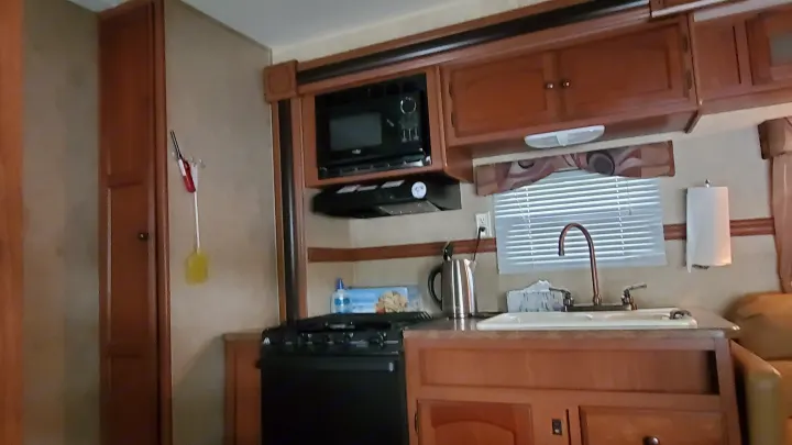Inside an RV rental: a well-equipped kitchen features a black stove, microwave, sink, and ample wood cabinetry.. Dutchmen Dutchmen 2012