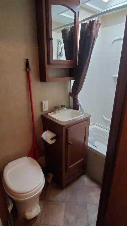 Inside an RV rental: a compact bathroom with a small toilet, sink, shower, and mirrored medicine cabinet. Tiled floor visible.. Dutchmen Dutchmen 2012