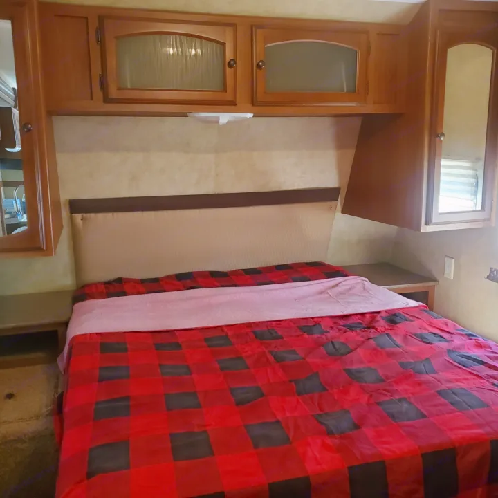 RV rental bedroom featuring a cozy red & black plaid bed, padded headboard, & ample wooden cabinets.. Dutchmen Dutchmen 2012