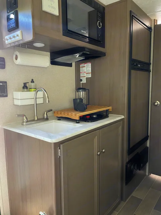 Step inside this RV rental's well-equipped kitchen featuring a sink, microwave, fridge, and portable stove.. Forest River Independence Trail 2021