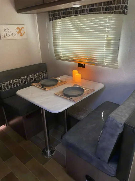 Inside an RV rental, a cozy dining booth with a set table, complete with two placesettings and flickering LED candles.. Forest River Independence Trail 2021