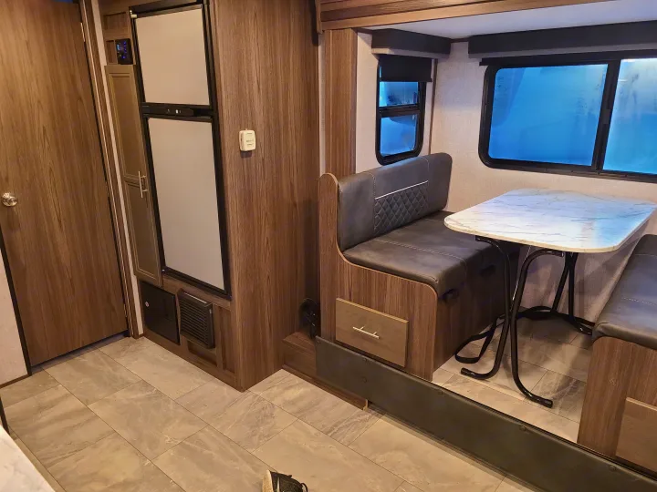RV rental interior showcases a functional dinette with storage, refrigerator, and bright windows for comfortable living.. Dutchmen Kodiak 2021