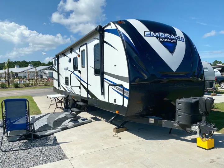 White & blue Embrace Ultra-Lite RV rental at a sunny campsite. This travel trailer's outdoor setup provides comfort.. Other Other 2018
