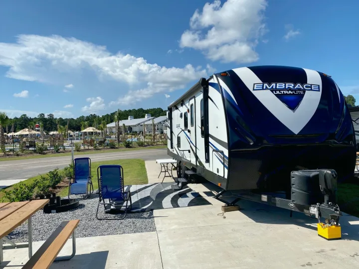 Spacious RV rental at a sunny resort campsite. Features a travel trailer, picnic table, chairs, and fire pit.. Other Other 2018