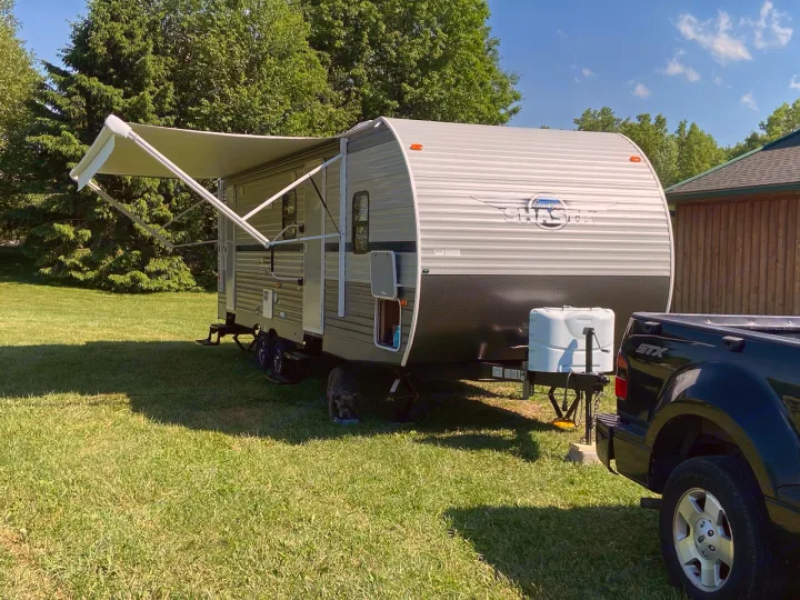 Enjoy your RV rental! A travel trailer with awning extended, hooked to a truck, set in a sunny, grassy camping spot with a dog.. Shasta Oasis 2019