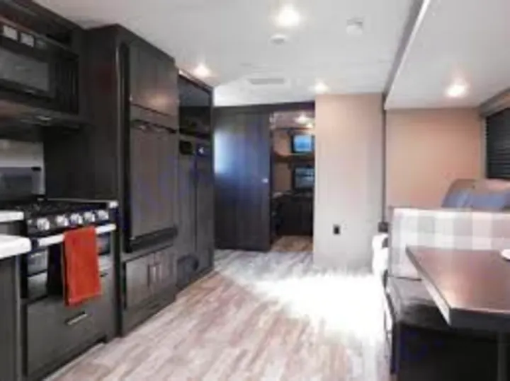 Spacious RV rental interior with a modern dark wood kitchen, light flooring, and a comfortable dinette area.. Grand Design Other 2021