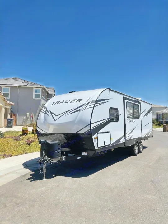 A sleek white Tracer travel trailer (RV) with black accents, parked on a sunny residential street. Great for an rv rental adventure!. Prime Time Tracer 2021