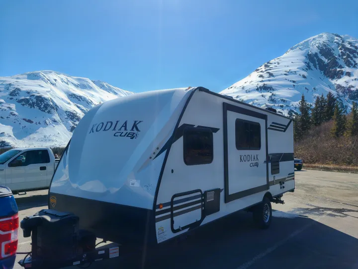 Kodiak Cub RV rental: a white travel trailer parked before stunning snow-covered mountains under a clear blue sky.. Dutchmen Kodiak 2021