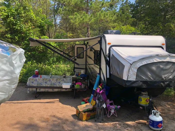 An RV rental set up at a sunny campsite with a picnic table & camping gear, ready for outdoor adventure.. Starcraft Launch 2018