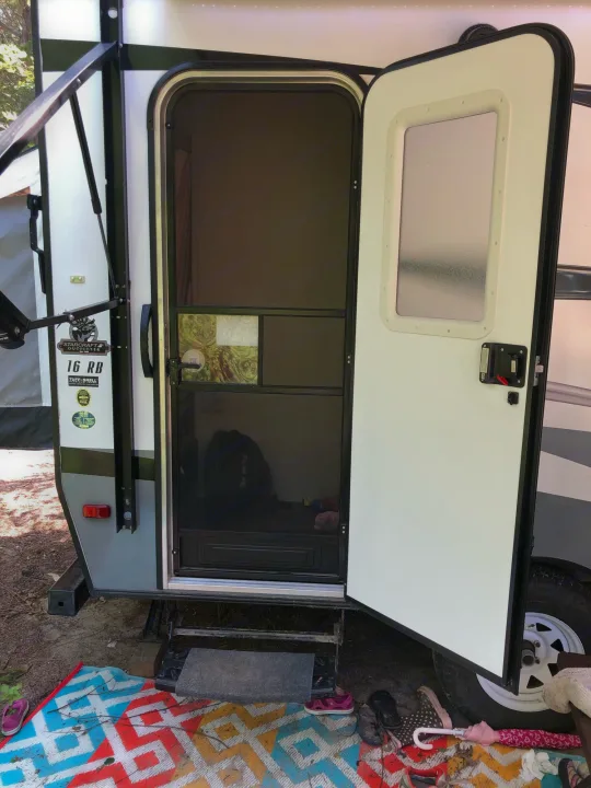 Open door of an RV rental showing the screen door, steps, and colorful outdoor mat with shoes and an umbrella.. Starcraft Launch 2018