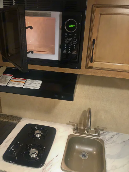Compact RV rental kitchen featuring an open microwave, a two-burner stovetop, and a small sink.. Starcraft Launch 2018