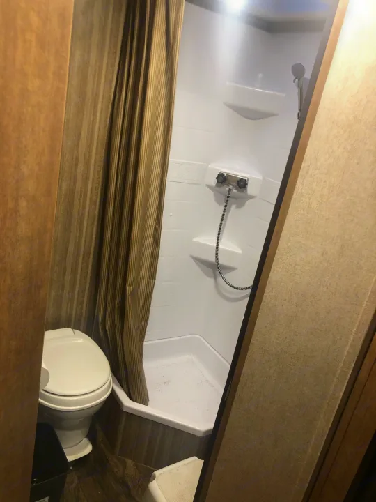 Compact RV rental bathroom with a toilet and corner shower, separated by a striped curtain.. Starcraft Launch 2018