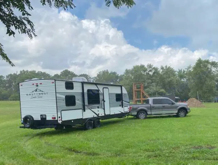 A gray pickup truck tows an East-West travel trailer on a green field, ready for an RV rental outdoor adventure.. East to West Della Terra 2021