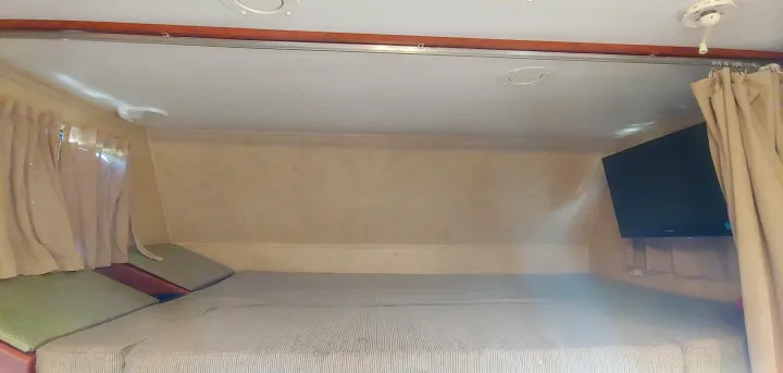 Inside an rv rental: a comfy overhead bunk with a striped mattress, wall-mounted TV, and side curtains.. Forest River Sunseeker 2012