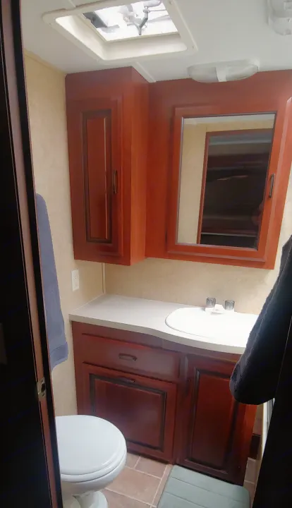 Experience comfort in this RV rental bathroom, featuring a clean toilet, vanity with sink, mirror, and ample storage.. Forest River Sunseeker 2012