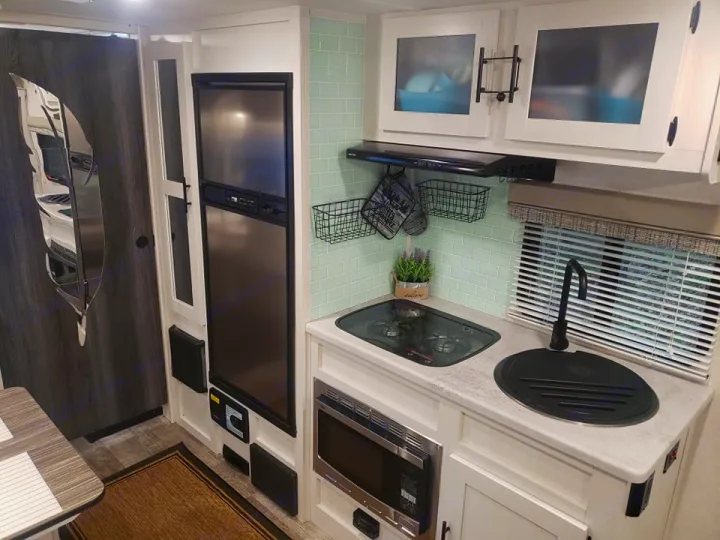 Inside an RV rental: a modern, compact kitchen with light green backsplash, stovetop, sink, and fridge visible.. Forest River R-Pod 2022
