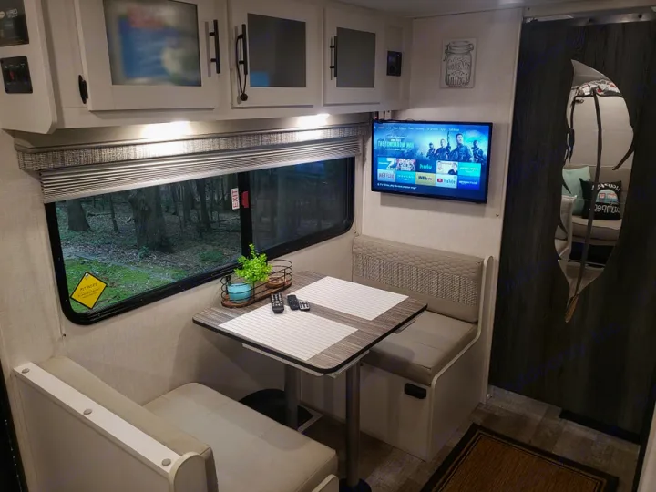 Inside an **rv rental**: a compact dinette with a window view of the woods, TV, and overhead cabinets, perfect for camping.. Forest River R-Pod 2022