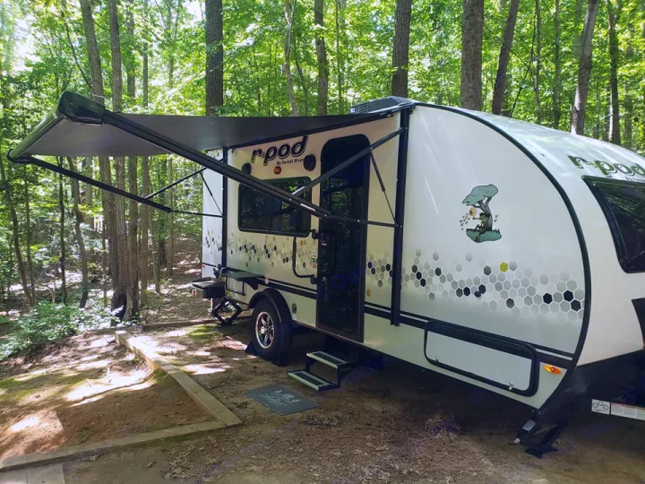 White r-pod RV rental under a deployed awning in a shady forest campsite. Features honeycomb patterns & tree decal.. Forest River R-Pod 2022