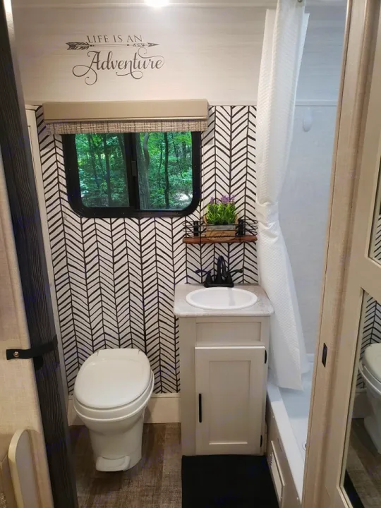 This stylish RV rental bathroom features a modern design, herringbone wallpaper, and a cozy window view. Perfect for your adventure!. Forest River R-Pod 2022