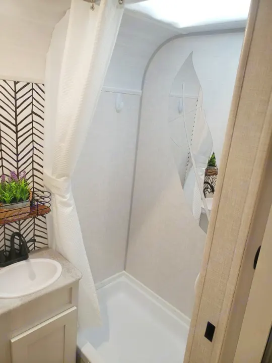 Compact RV rental bathroom: sink, shower with a pulled-back curtain, and a unique clear, leaf-shaped liner. Bright interior.. Forest River R-Pod 2022