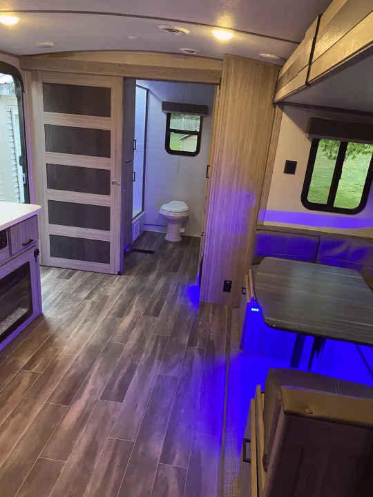 Spacious RV rental interior featuring a modern kitchen, bathroom, and dinette, accented by vibrant blue LED lighting.. Keystone Passport 2021