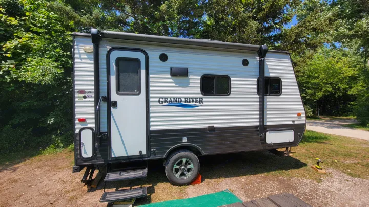 A white and black travel trailer, perfect for an RV rental, is parked at a scenic campsite surrounded by lush green trees.. Forest River 16RB 2019
