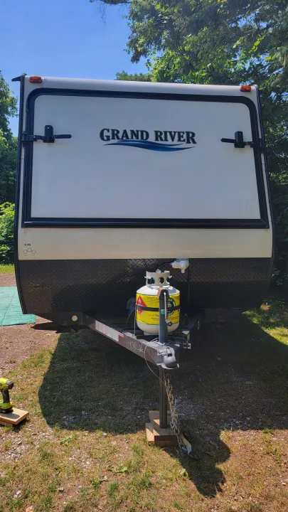 Upright view of a white "Grand River" travel trailer's front. Propane tank and hitch visible. Perfect for an rv rental adventure.. Forest River 16RB 2019