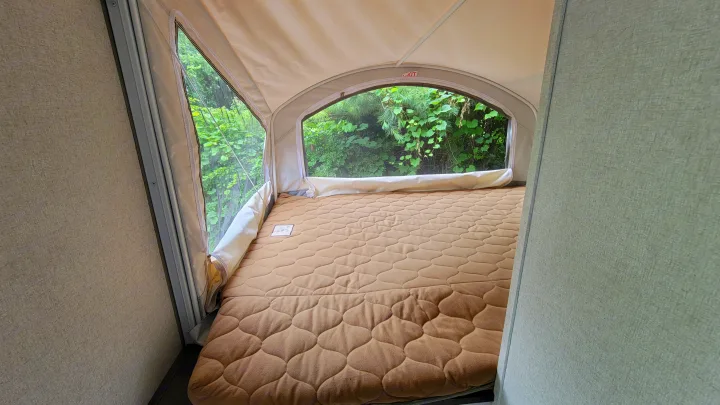 Cozy bed in an RV rental's pop-out bunk, with canvas interior and clear view of green nature outside.. Forest River 16RB 2019