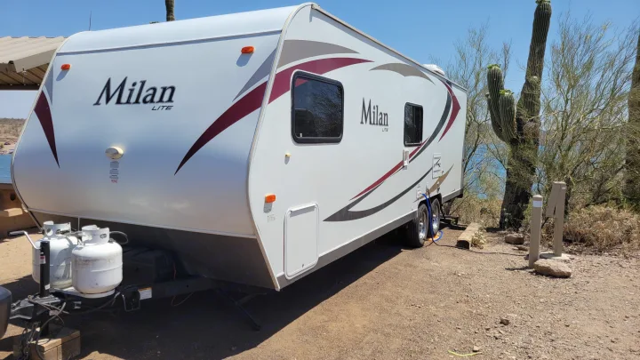 A white Milan travel trailer RV rental is parked at a desert campsite by a lake, surrounded by saguaro cacti.. Eclipse Recreational Vehicles Milan 2013