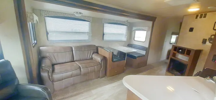 Explore this rv rental's inviting living space: a comfy sofa, dining booth, windows with blinds, and a built-in fireplace.. geo 267RL 2018