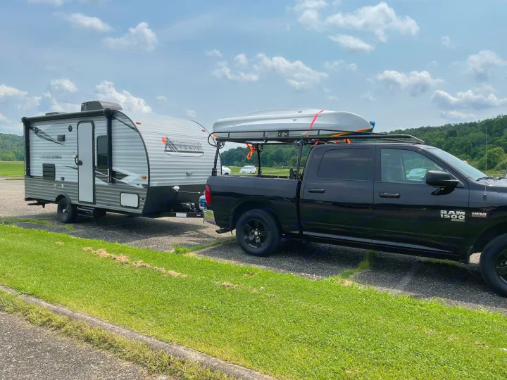 Black truck towing an RV rental. A kayak sits on the truck's bed rack, parked in a paved lot.. Forest River Independence Trail 2021