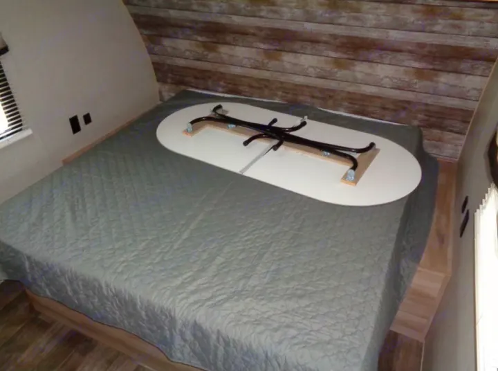 RV rental bedroom with a bed & multi-functional table stowed upside down. Smart space-saving design for a camper.. Coachmen Catalina 2021