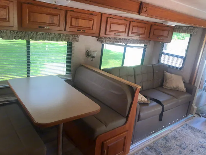 RV rental interior showcasing light brown dinette seating, a matching sofa with a pillow, and wood cabinets.. Damon Daybreak 2005
