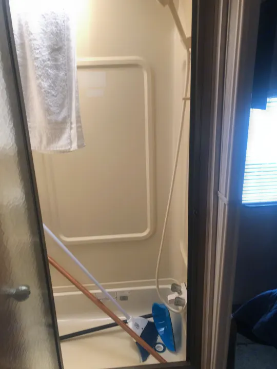 Inside an RV rental shower, a white broom and blue dustpan are stored. A white towel hangs nearby, reflecting light.. Damon Daybreak 2005